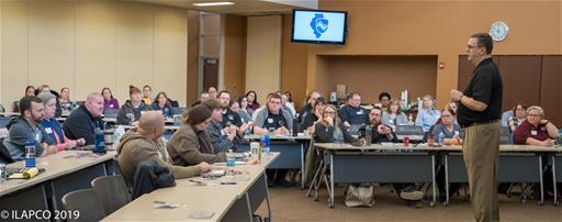 Man Speaking to People Sitting at Long Tables